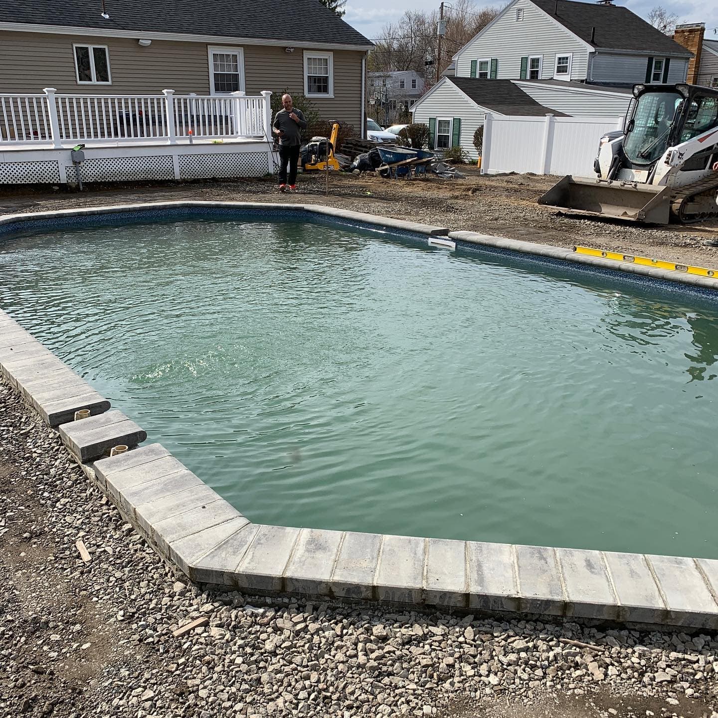 New coping going in around a pool, with a skid steer working nearby