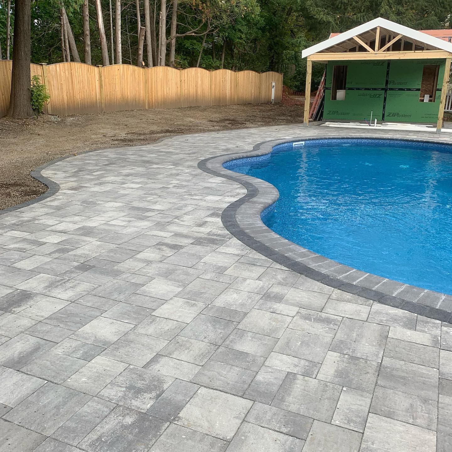 Kidney-shaped pool with a gray paver deck and dark coping built by M&M