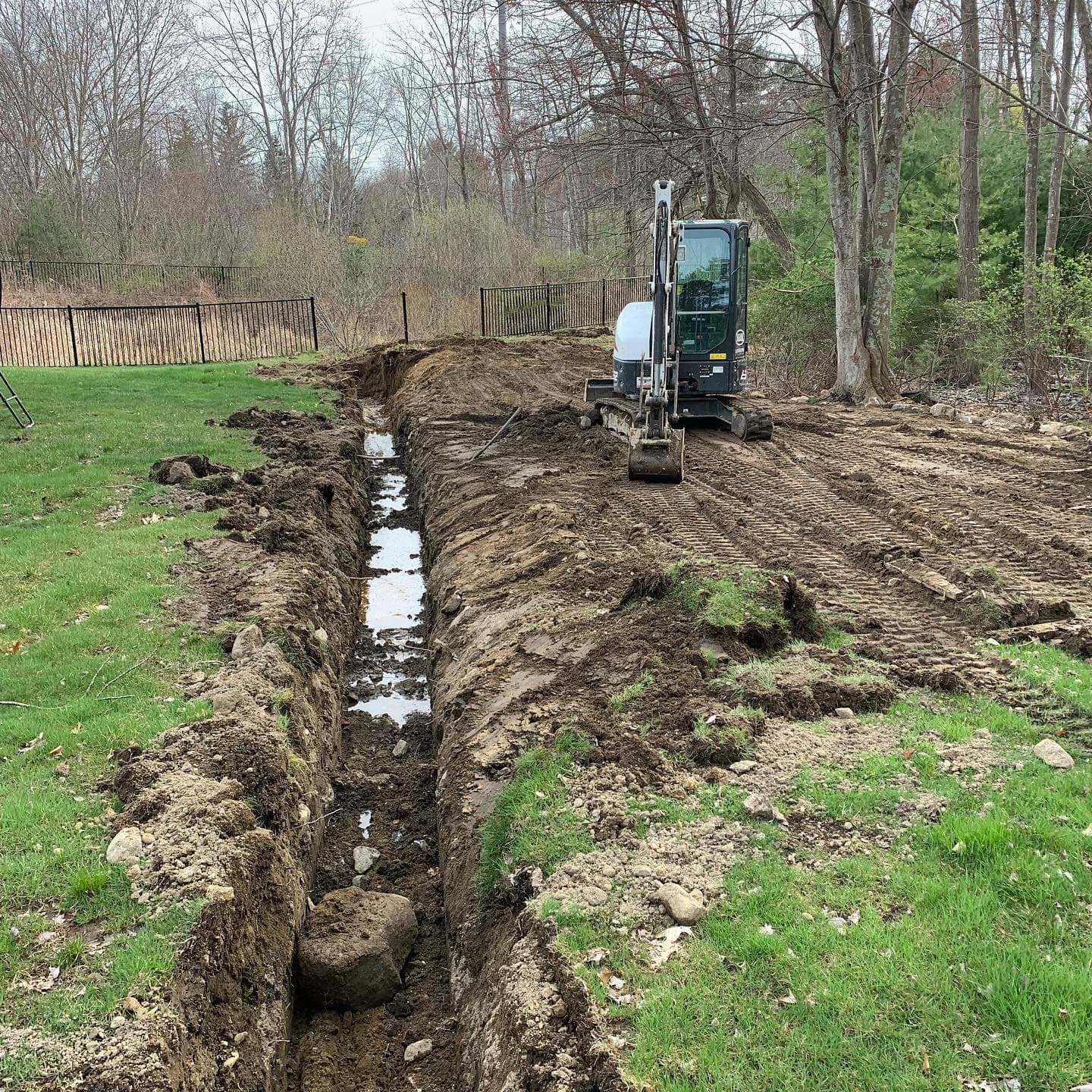 Excavator digging a long drainage trench across a wet yard